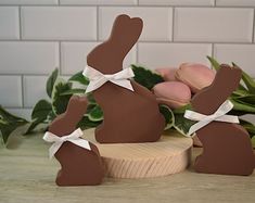 two chocolate bunny figurines sitting on top of a wooden table next to flowers