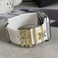 an apple watch with gold and white bracelets on top of the strap, sitting on a carpeted surface