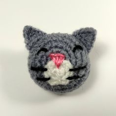 a crocheted gray cat head with pink nose and white chest, on a white background