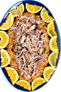 a blue plate topped with meat and rice covered in orange slices next to sliced lemons