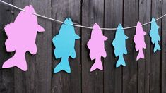 paper cutouts of fish hanging from a line on a wooden fence in front of a wood wall