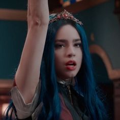 a woman with blue hair wearing a tiara and raising her arm in the air