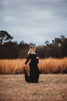 a pregnant woman in a black dress sitting on the ground with her hands behind her back