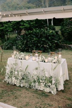 a table with candles and flowers on it in the middle of a field near some trees