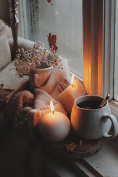 some candles are sitting on a window sill next to a coffee cup and sweater