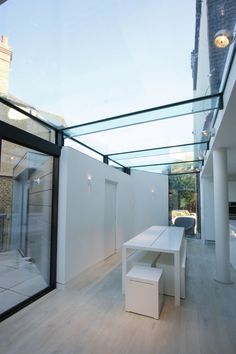 a white table sitting on top of a wooden floor next to a glass roof over an outdoor kitchen