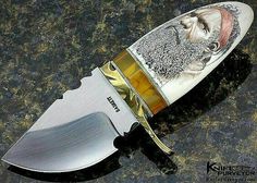 a knife that is sitting on top of a table with a painting on it's blade