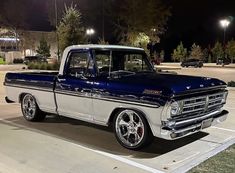 an old blue and white truck parked in a parking lot next to some buildings at night