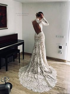 a woman standing in front of a piano wearing a wedding dress with long sleeves and open back