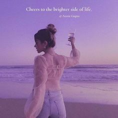 a woman standing on top of a beach next to the ocean holding a glass of wine