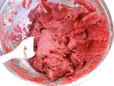 a mixing bowl filled with red food on top of a wooden table