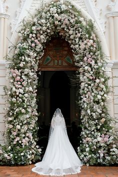 a bride standing in front of an archway with flowers