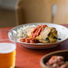 a white plate topped with meat and rice next to a glass of beer on a table