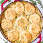 a casserole dish filled with biscuits and vegetables on a white table cloth next to green sprigs