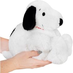 a hand holding a white stuffed dog with black ears and tail, in front of a white background