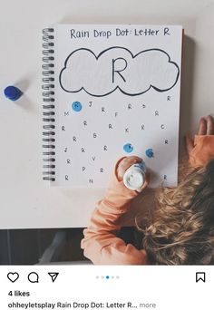 a child is holding up a notebook with rain drop dot letter r written on it