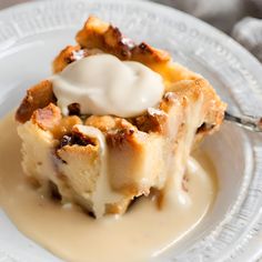 a piece of bread pudding on a white plate with cream drizzled over it