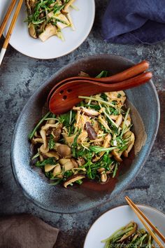 two plates with stir fry vegetables and chopsticks in them on a blue table