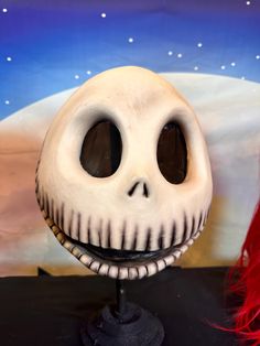 a doll with red hair and a fake skeleton face on it's head in front of a painting