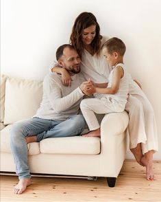 a man, woman and child sitting on a white couch with their arms around each other