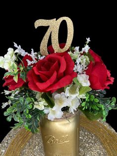 a gold vase filled with red roses and white flowers on top of a table next to a golden plate