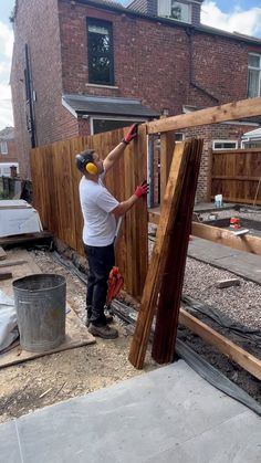 a man working on a wooden fence in front of a brick building with construction tools