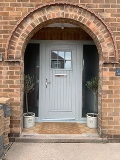 a grey front door with two planters on either side and an arched brick wall