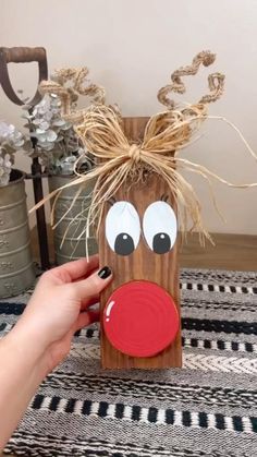 a hand holding a piece of wood with a reindeer head on it and eyes painted red