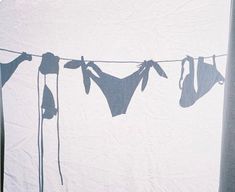 clothes hanging on a line in front of a white wall with the shadow of two bikinisuits hung to dry