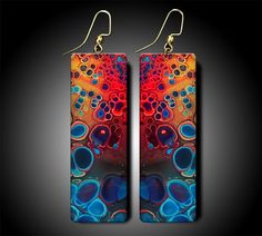 pair of earrings with an abstract design on them, sitting against a black background and hanging from gold earwires