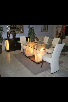 a glass dining table with white chairs and lights on the top, in a living room