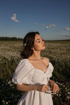 a woman in a white dress is standing in a field with daisies and looking off into the distance