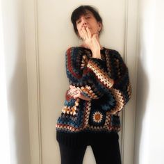 a woman standing in front of a white door with her hands on her face while wearing a crocheted sweater