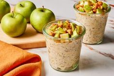 three glasses filled with oatmeal sitting on top of a table next to green apples