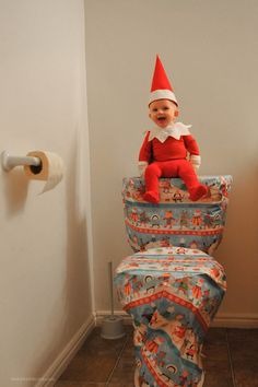 a baby sitting on top of a toilet seat wearing a red and white elf hat