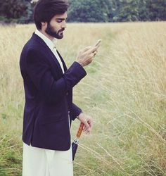 a man in a suit is looking at his cell phone while standing in the grass