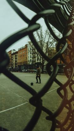 a man is playing with a ball in an open area next to a fence and some buildings