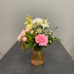 a vase filled with lots of flowers on top of a black counter next to a wall