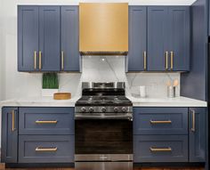 a kitchen with blue cabinets and white counter tops, gold trim on the oven hood