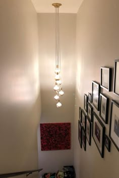 the light fixture is hanging from the ceiling above the stairs in this hallway with pictures on the wall