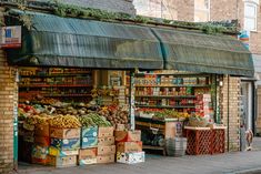 an outdoor market with lots of fruits and vegetables on the outside, in front of a brick building