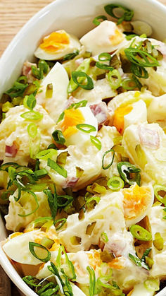 a white bowl filled with potato salad on top of a wooden table