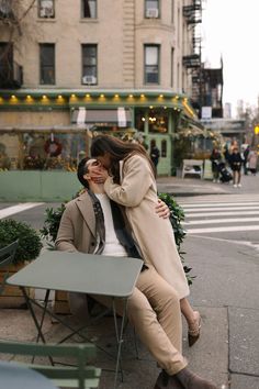 two people sitting on a bench in front of a building and one is hugging the other