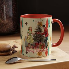 a red and white coffee mug sitting on top of a wooden table next to a spoon