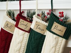 three christmas stockings hanging from a mantel with name tags attached to them and evergreens in the background