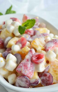 a white bowl filled with fruit salad on top of a table next to a green leaf