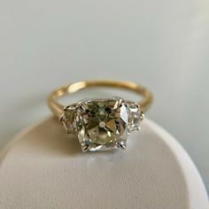 three stone ring sitting on top of a white display stand with an oval cut diamond in the center