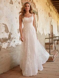 a woman in a white wedding dress standing on a brick floor next to a wall