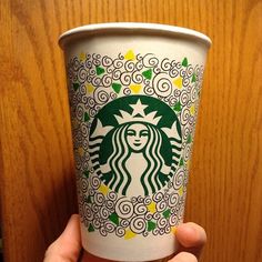 someone holding up a starbucks cup in front of a wooden wall with swirly designs on it