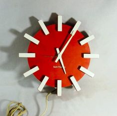 a red clock with white sticks sticking out of it's face on a wall